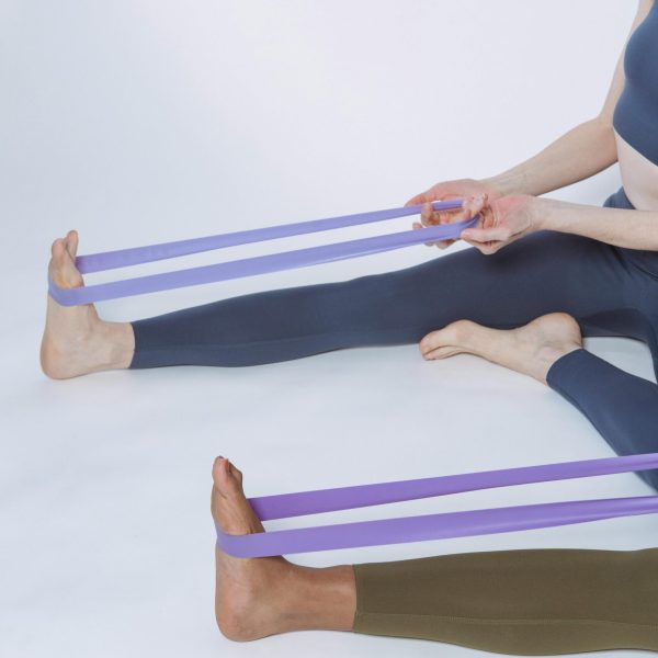 Two women using purple resistance bands for a fitness workout in a studio setting.