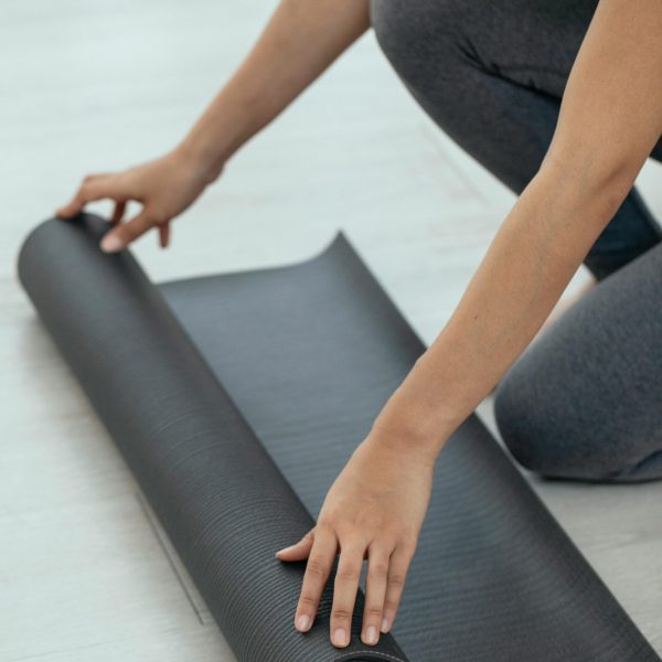 A woman unrolling a yoga mat indoors, preparing for a fitness workout.